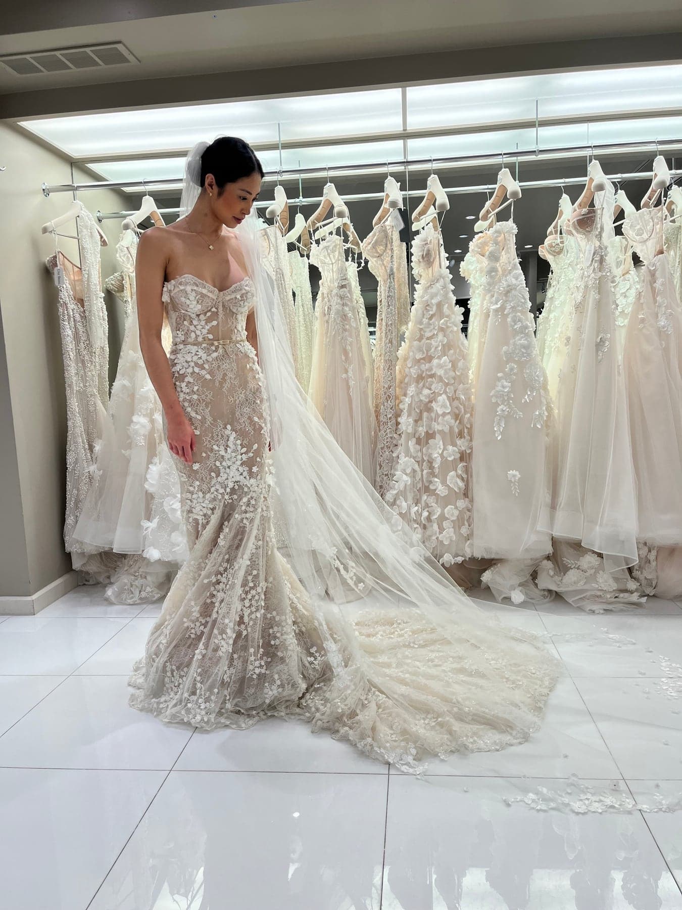 Bride in a floral lace gown with the train fanned out across a white salon floor