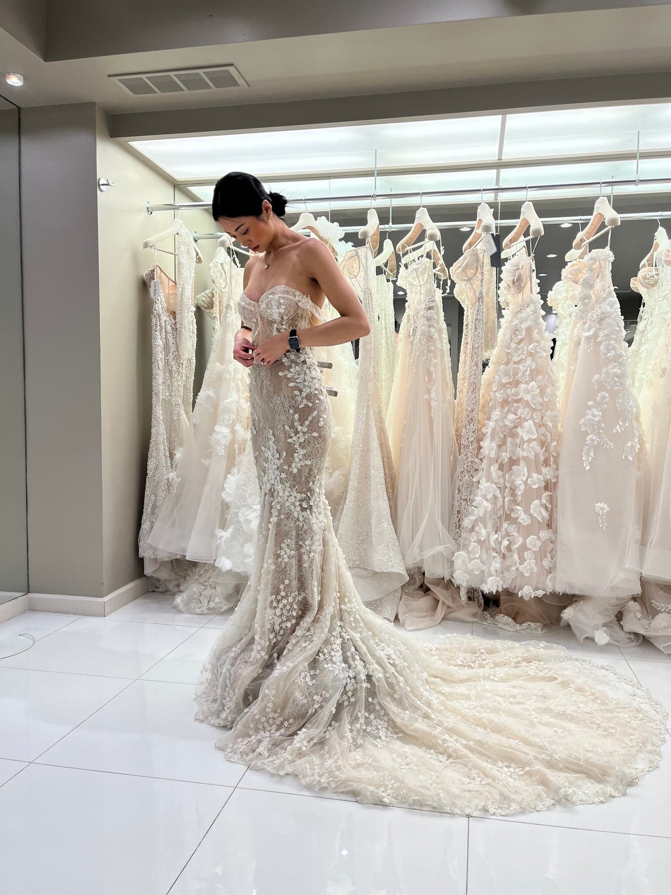 Bride adjusting the bodice of a lace gown in front of a rail of dresses